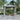 Gray outdoor gazebo with side curtains and open center, set in a garden among plants.