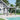 Gray outdoor gazebo with side curtains and open roof, standing on four legs over patio.